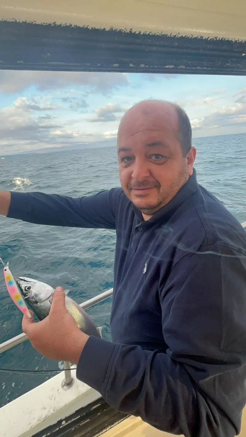 Tekne güvertesinde tuttuğu balığı gösteren bir balıkçı